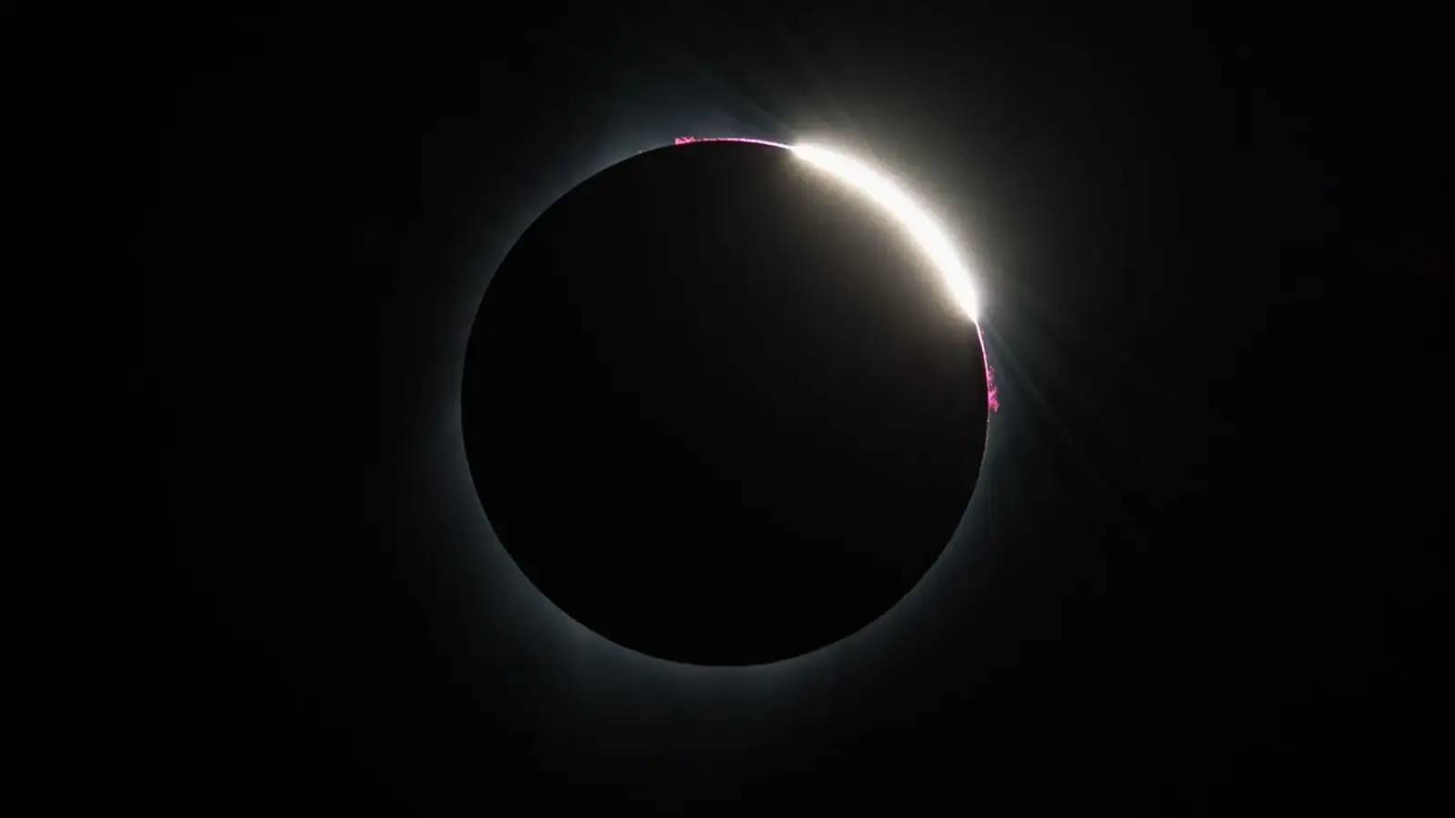 The Moon moving off the Sun after totality, revealing a bright solar crescent and pink prominences during the 2017 eclipse